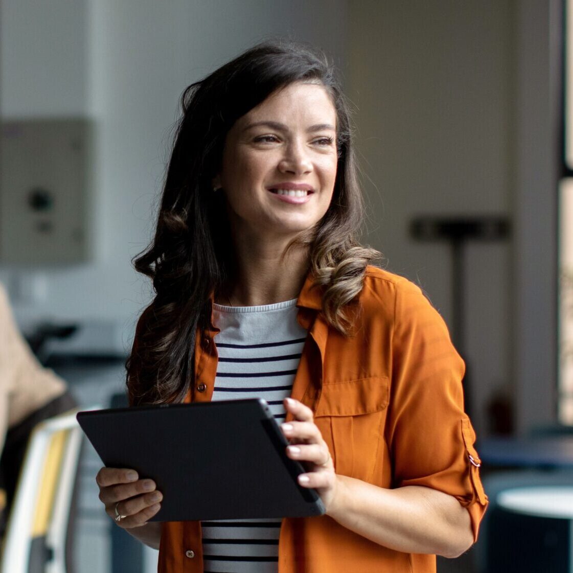 Mid adult female businesswoman standing and walking through modern office while her colleagues working and brainstorming